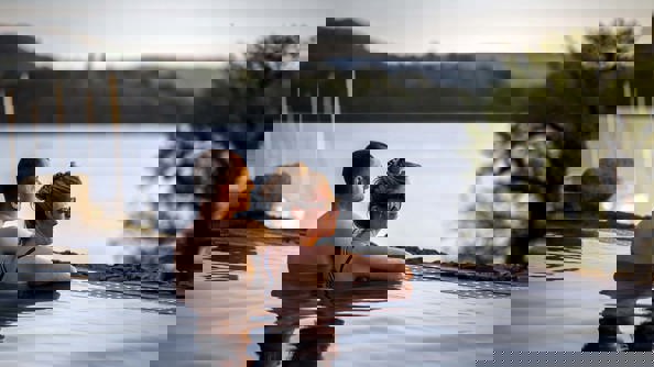 Two people in Low Wood Bay's outdoor Vitality Pool overlooking Lake Windermere at Sunset